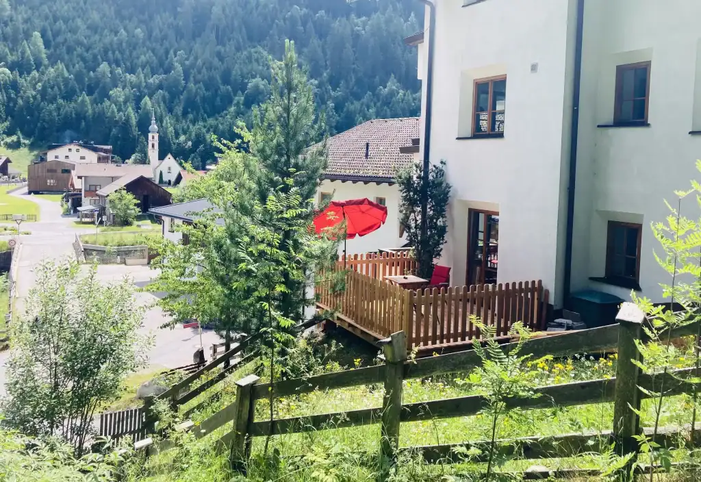 Balkon mit rotem Sonnenschirm und Garten, umgeben von Natur und Bergen in Slois.