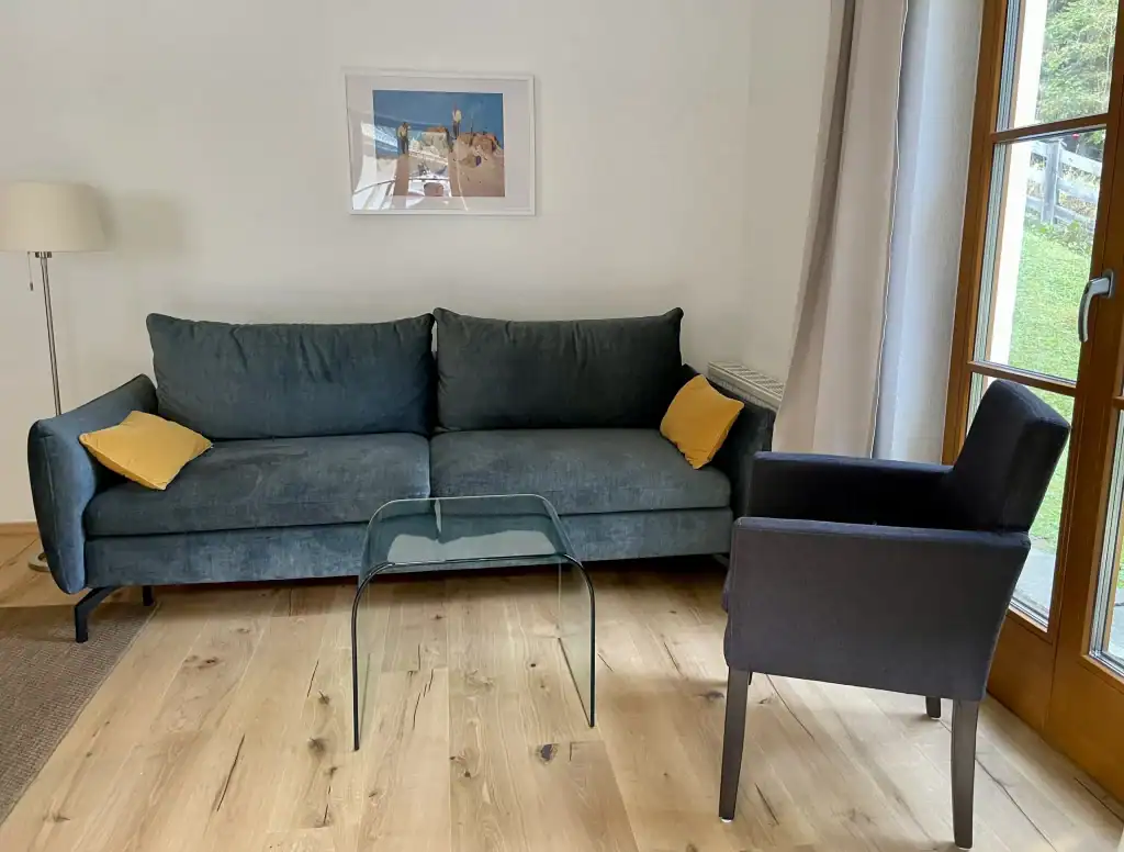 Gemütliches Wohnzimmer mit Sofa, Sessel und großem Fenster.