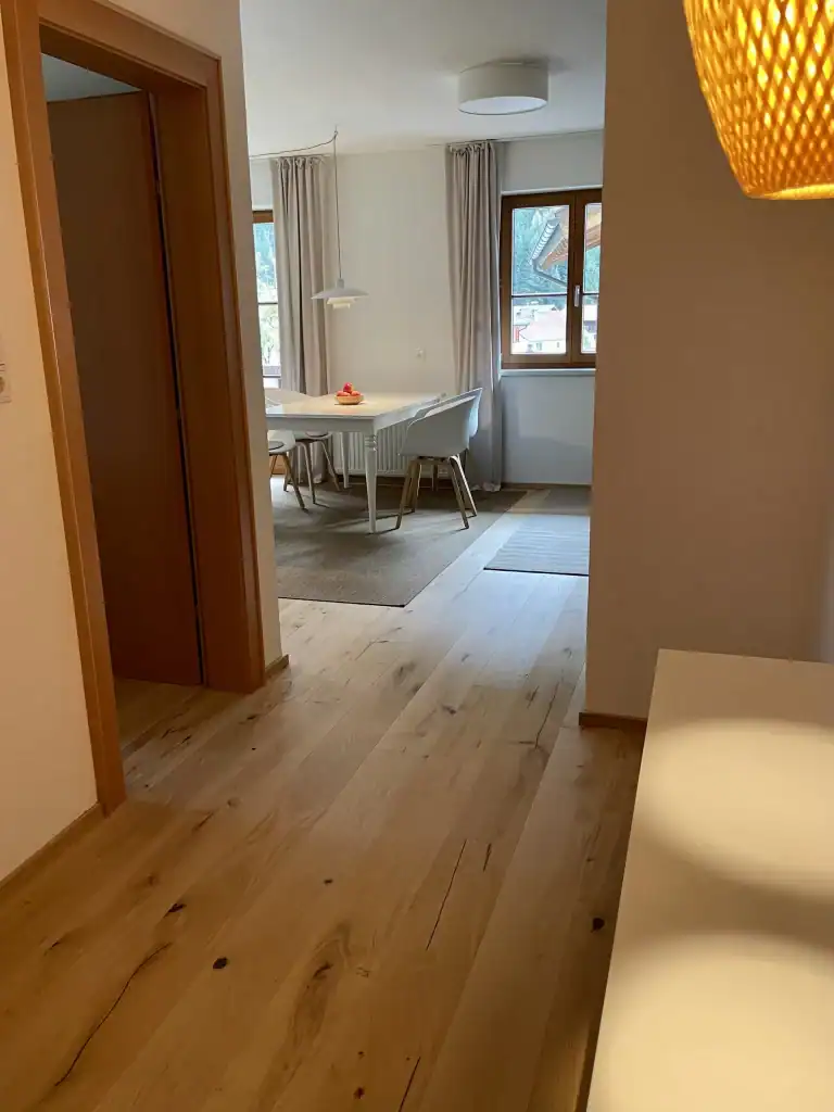 Helles Wohnzimmer mit Essbereich, großen Fenstern und moderner Einrichtung in einer Ferienwohnung.