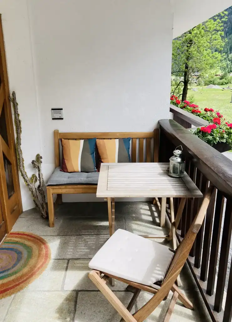 Gemütlicher Balkon mit Holzbank, Stühlen und Blick auf grüne Landschaft und Blumen.