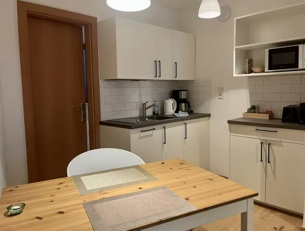 Moderne Küche mit weißen Schränken und Holzarbeitsplatte, Mikrowelle und Kaffeemaschine.