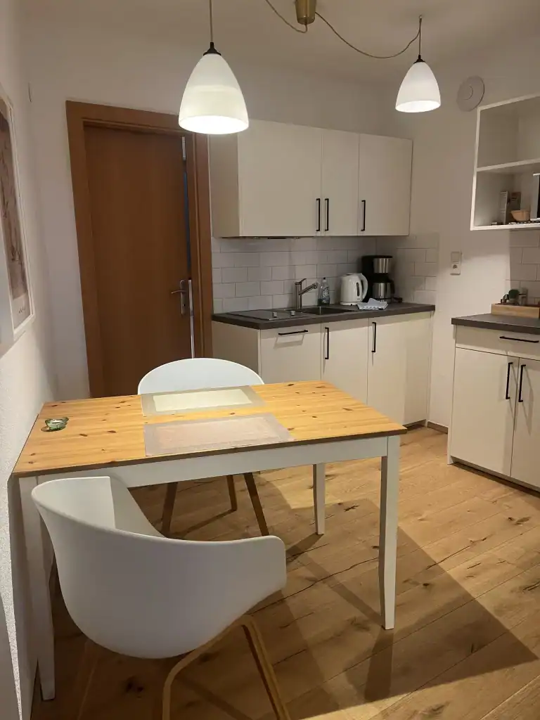 Kleines Kücheninterieur mit Esstisch, weißen Stühlen und moderner Küchenausstattung.