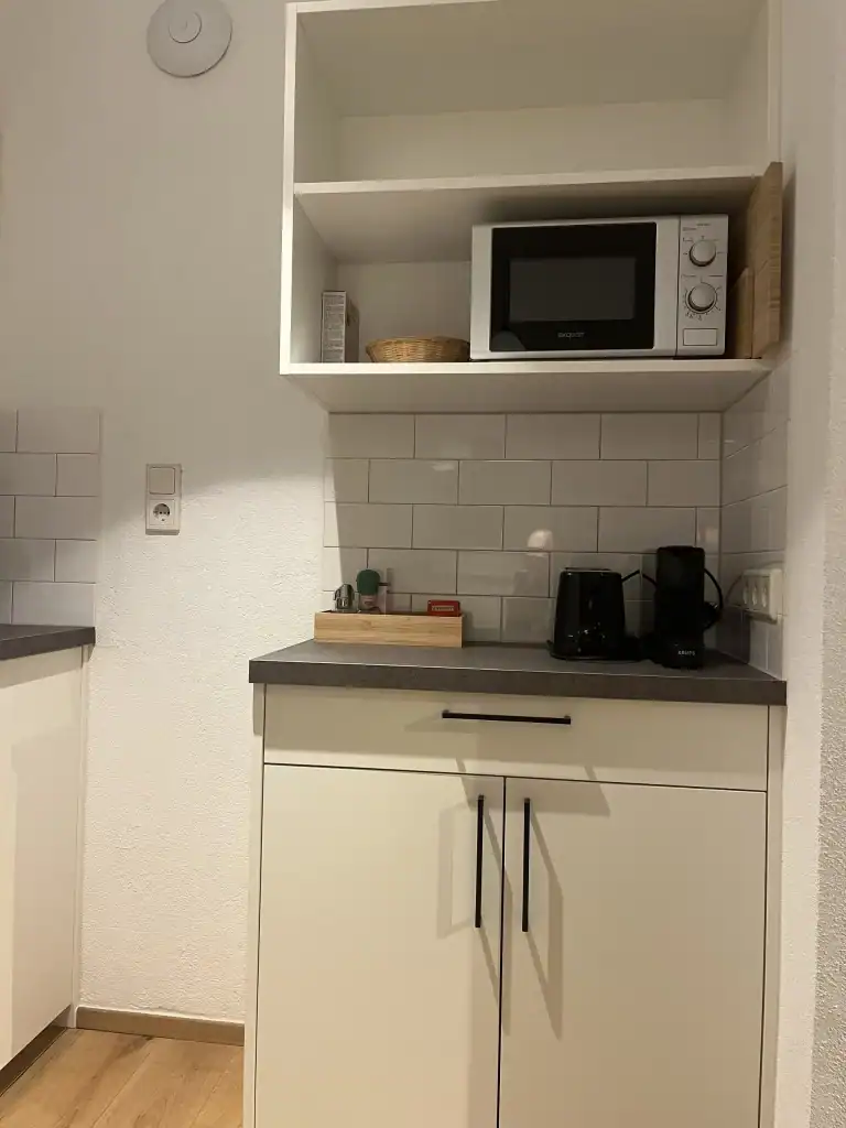 Küchenschrank mit Mikrowelle, Toaster und Küchenutensilien in moderner Küche.