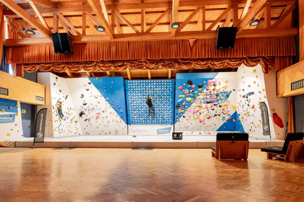 Indoor-Kletterwand im Quellalpin mit bunten Griffen und Kletterer.